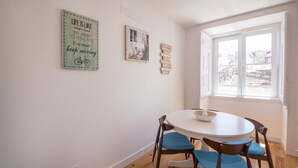 A dining area with a round table, blue cushioned chairs, and a window with a view of buildings. - Alfama Premium by Homing (Lisbon)