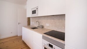 A modern kitchen with white cabinetry, a built-in microwave, a sink, and a stove. - Alfama Premium by Homing (Lisbon)