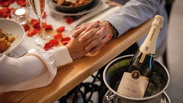 A person holding hands with another, a bottle of champagne in a bucket, and a plate of food on a table.