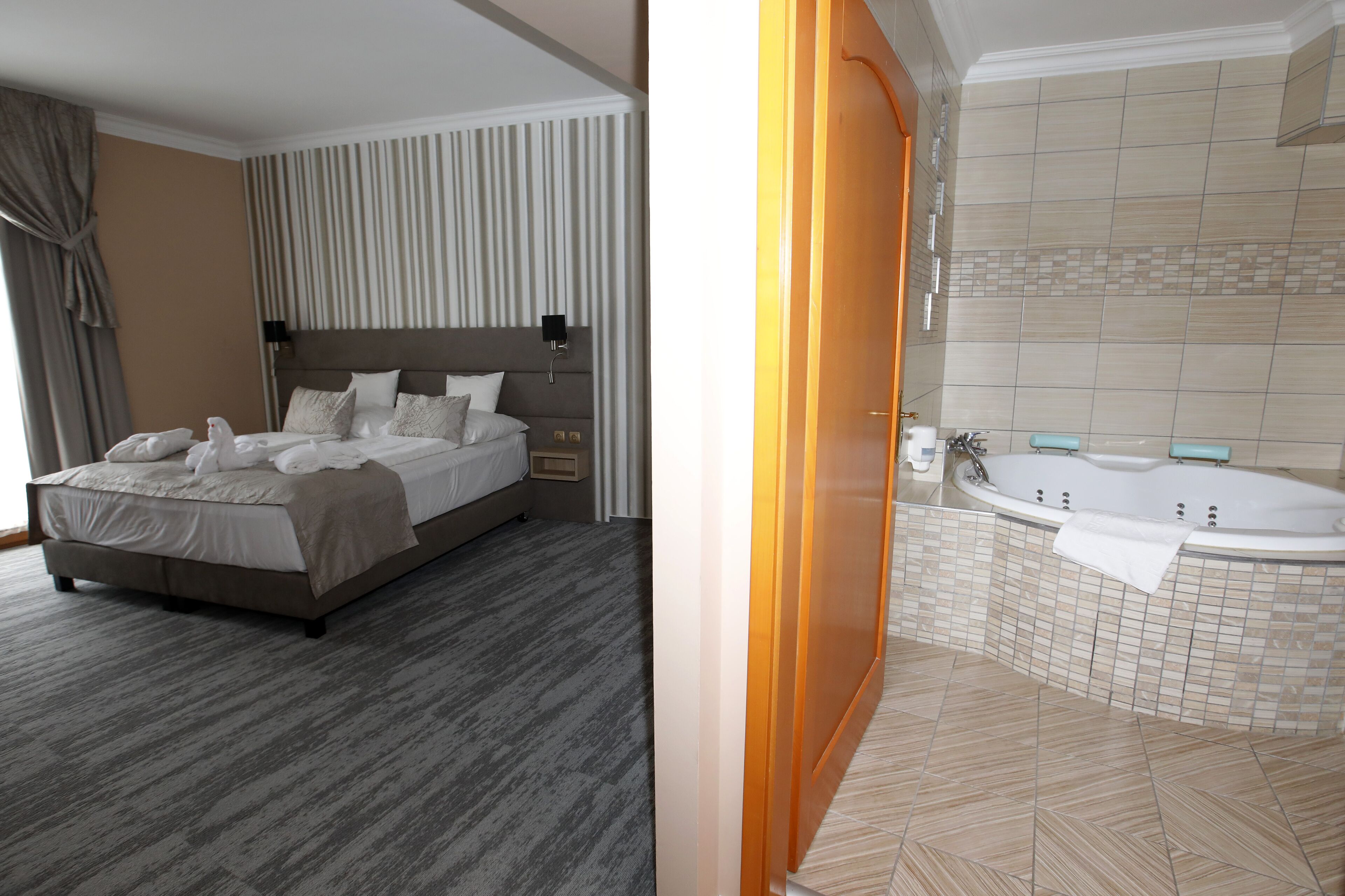 Une chambre d’hôtel avec un grand lit, une table de chevet, une commode et une salle de bain dotée d’une baignoire et de murs carrelés.