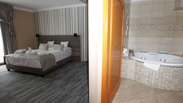 Une chambre d’hôtel avec un grand lit, une table de chevet, une commode et une salle de bain dotée d’une baignoire et de murs carrelés.