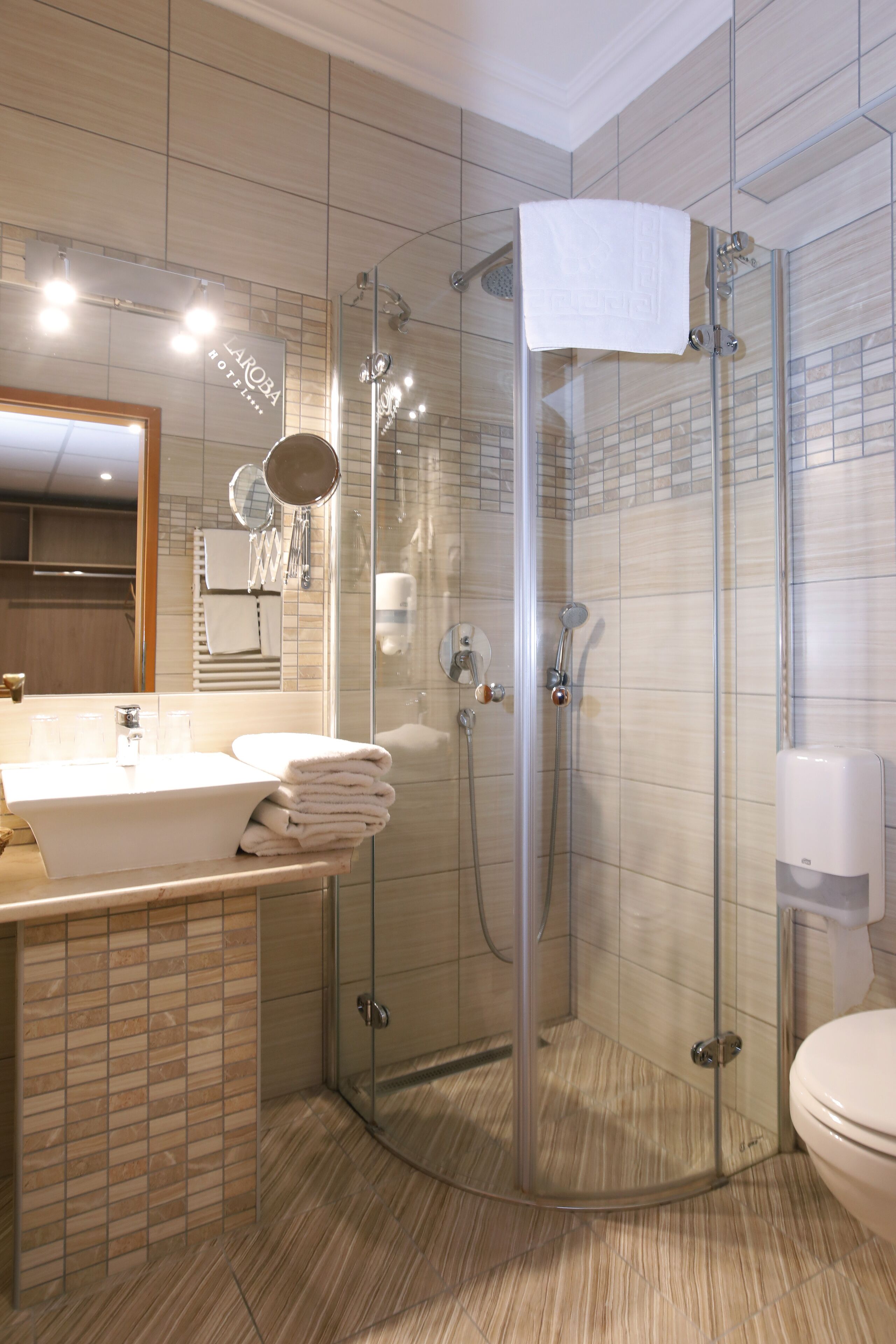 Un baño moderno con ducha envuelta en vidrio, un lavamanos con toallas apiladas y un inodoro.