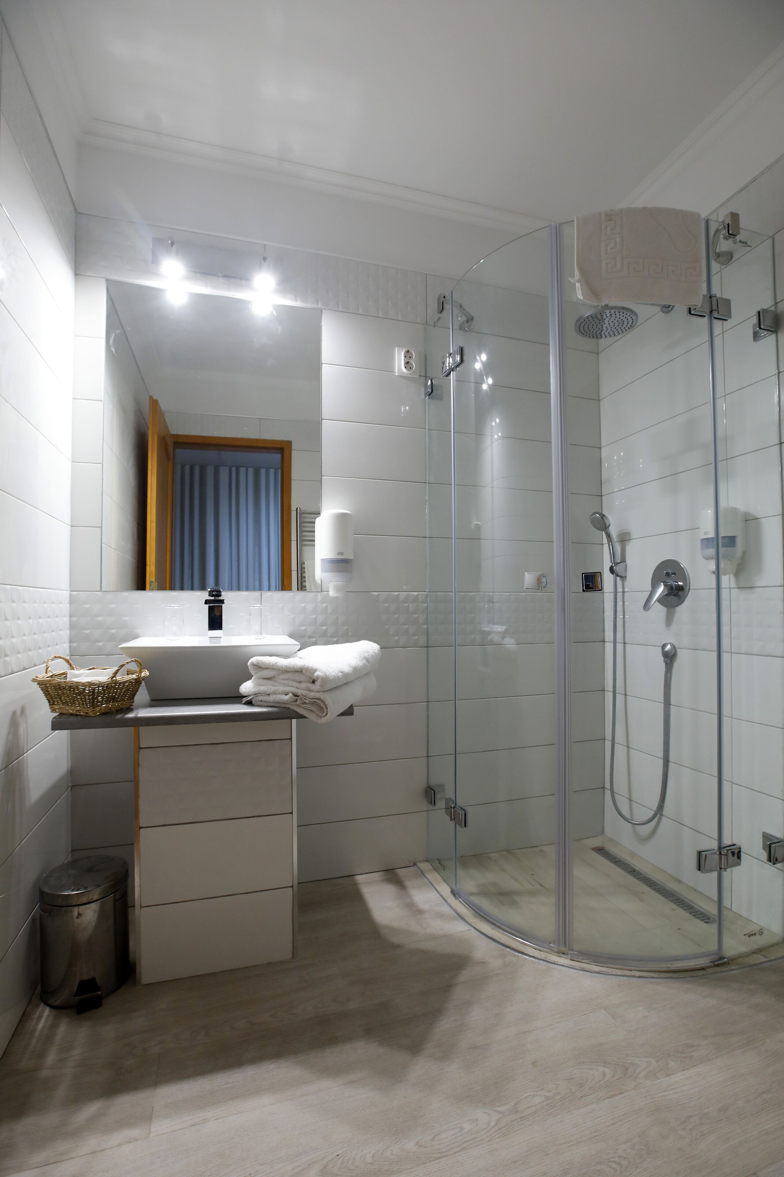 Ein modernes Badezimmer mit einer gläsernen Duschkabine, einem weißen Waschbecken und einer kleinen Mülleimer.