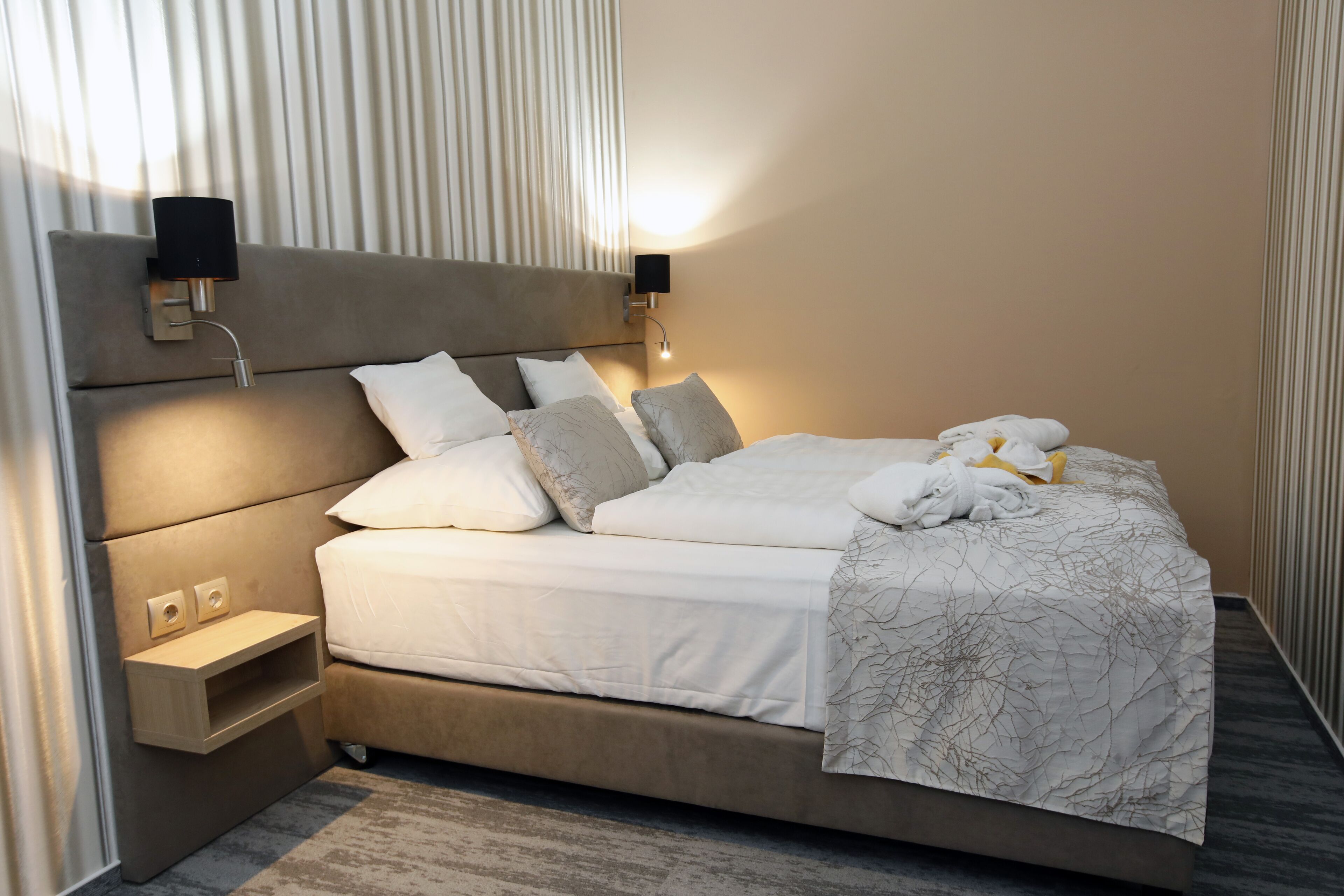Une chambre d’hôtel moderne avec un grand lit, deux tables de chevet et des lampes fixées au mur.
