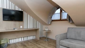 Un dormitorio tipo loft moderno con techo inclinado, un televisor de pantalla plana en la pared, un sofá gris y una pequeña mesa redonda con una lámpara.
