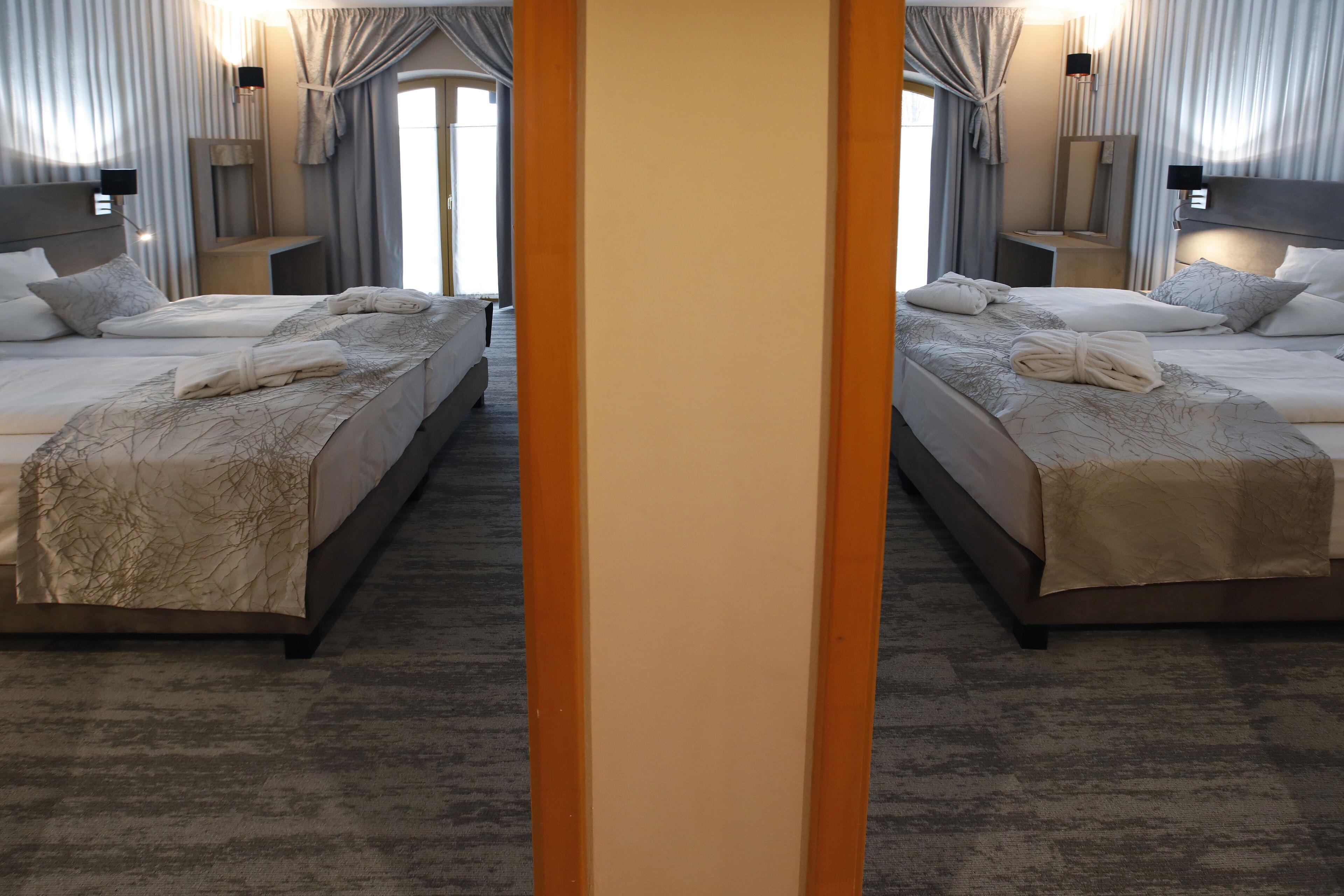 A mirrored hotel room with two beds, each with a headboard, bedside tables, and lamps.