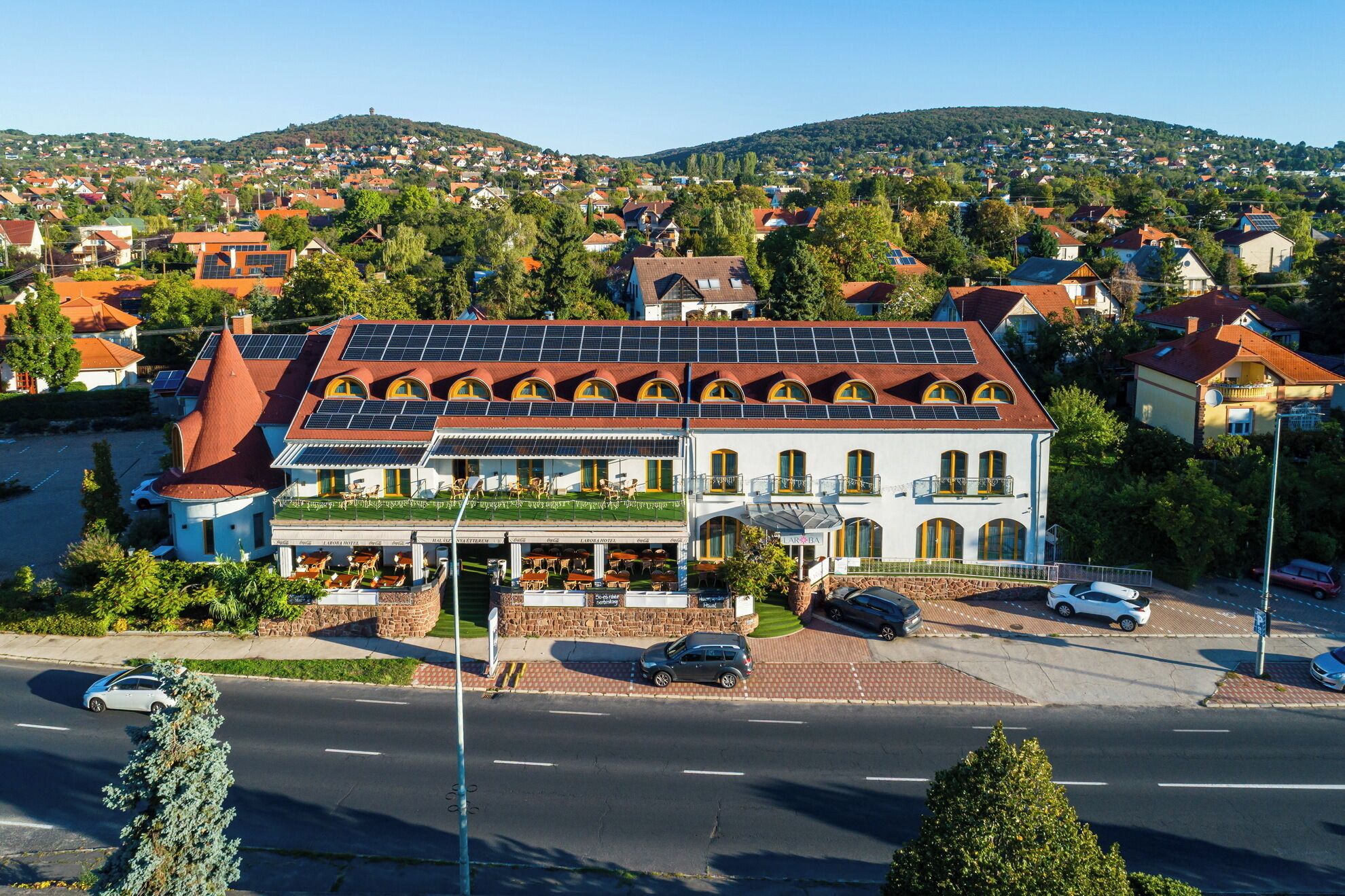 Een hotel met een rood dak, zonnepanelen en een restaurant op de begane grond.