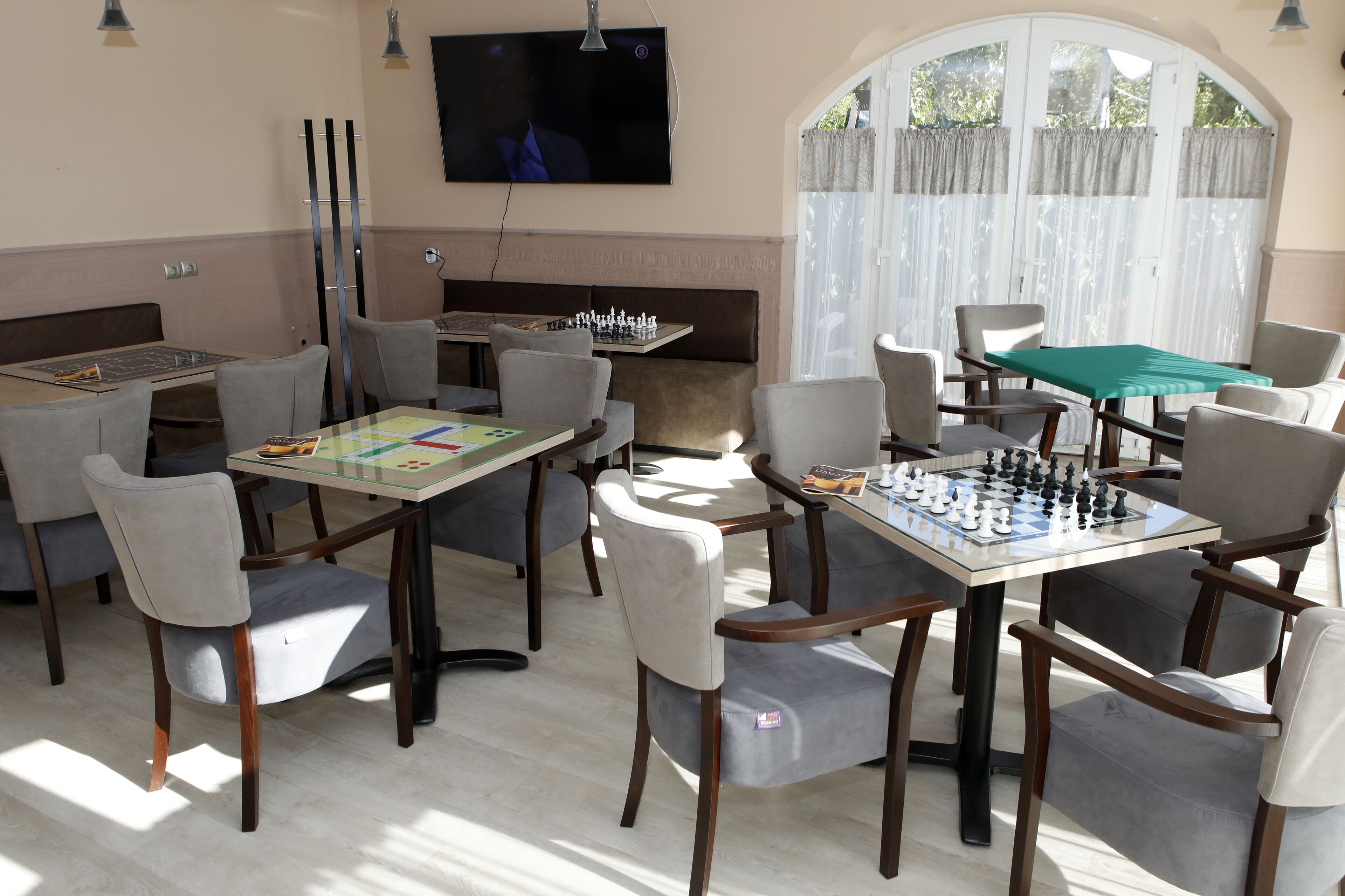 A room with multiple tables set up for games, a television mounted on the wall, and a large window with curtains.