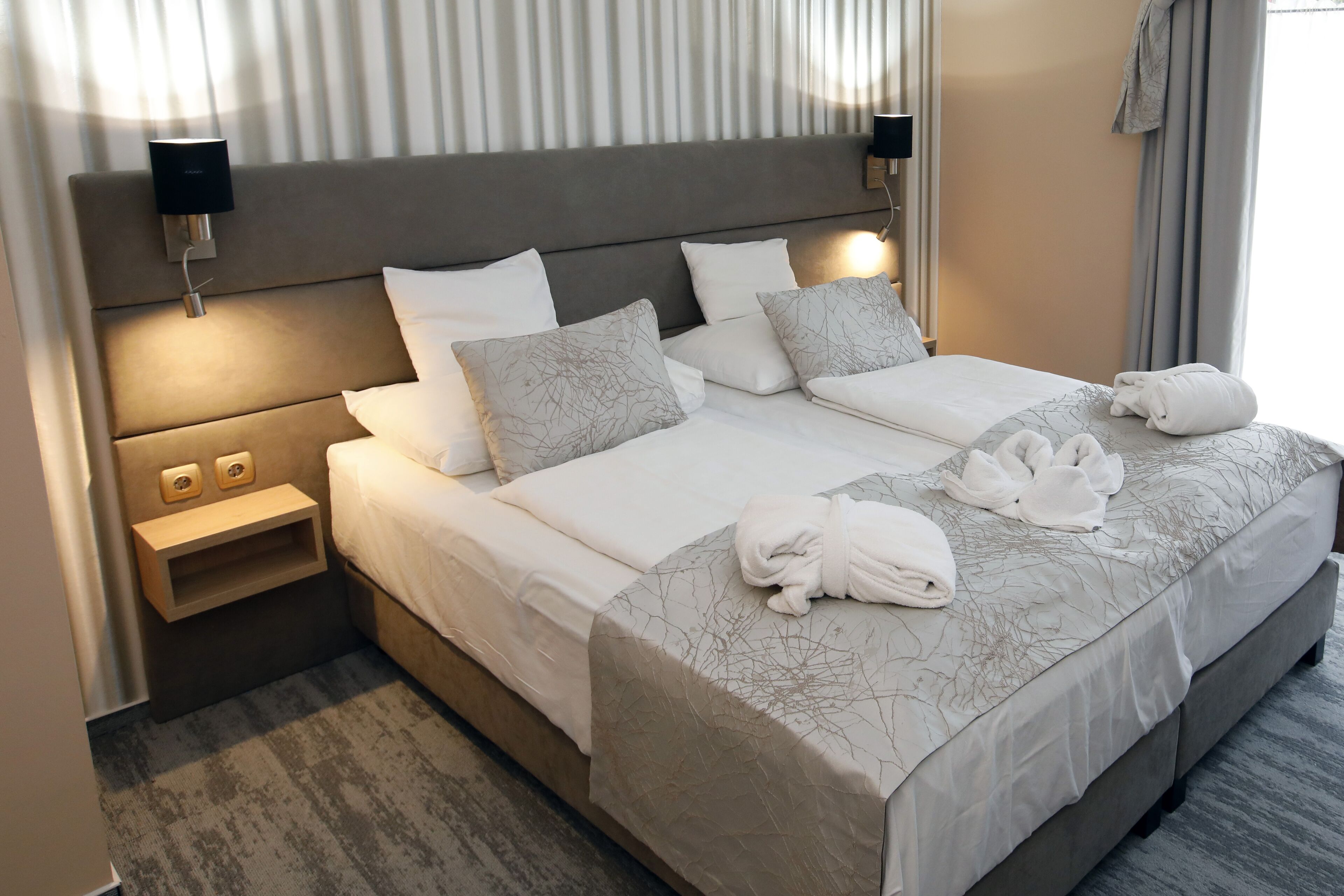 A neatly made double bed with a grey patterned bedspread, two bedside tables with lamps, and a headboard with integrated lighting.