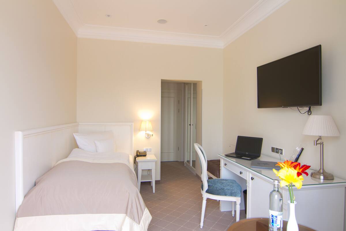 Ein Hotelzimmer mit Bett, Schreibtisch, Stuhl, Fernseher und einer Vase mit Blumen.