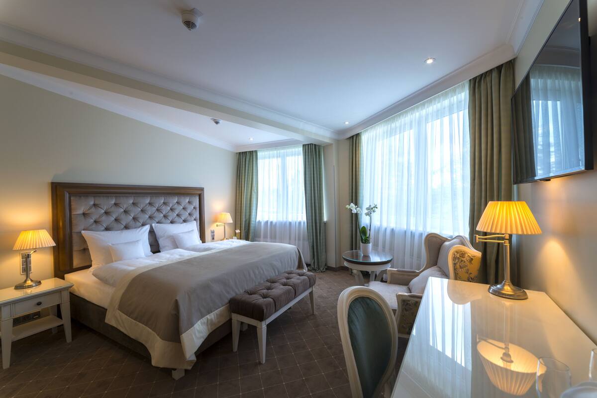 Ein Hotelzimmer mit einem großen Bett, Nachttischen, einer Bank, einem Schreibtisch mit Stuhl und einem Fernseher.