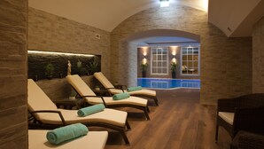 A spa area with reclining chairs, a stone wall, a small pool, and a window with plants. - Park Hotel & Spa Katharina (Badenweiler)