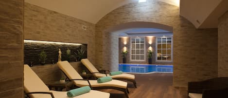 A spa area with reclining chairs, a stone wall, a small pool, and a window with plants.