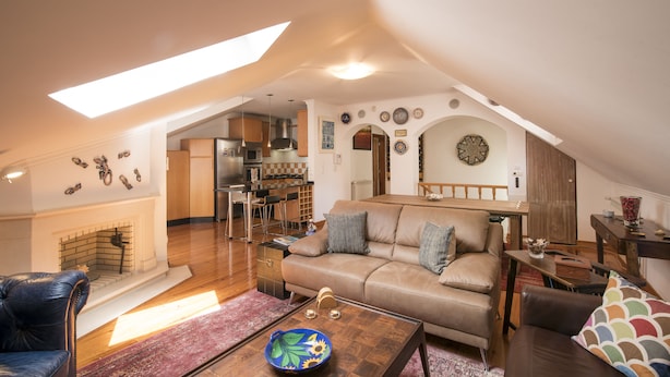 Una sala de estar acogedora con sofá, mesa de centro y chimenea. Hay un comedor con sillas y una mesa, y una cocina al fondo.