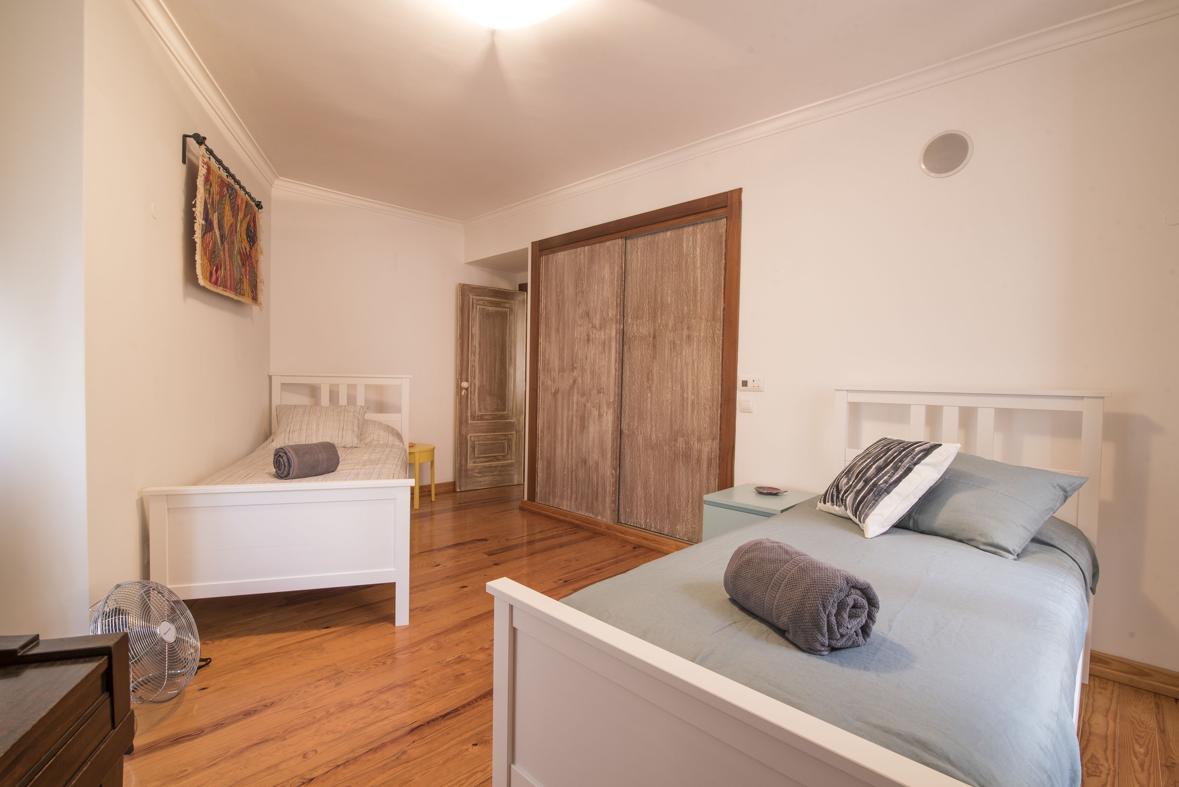 Ein Schlafzimmer mit zwei Betten, einem Holzschrank, einem kleinen Tisch und einem Ventilator.