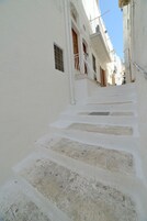 A narrow, white-walled alley with stone steps leading to a building with balconies.