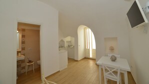 A spacious kitchen with a dining area, a small bathroom, and a TV mounted on the wall. - Casa Baldassarre (Ostuni)