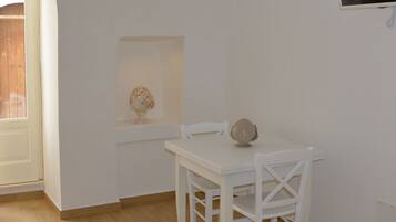 A small, white dining area with a table and chairs, a decorative item on the table, and a television mounted on the wall.