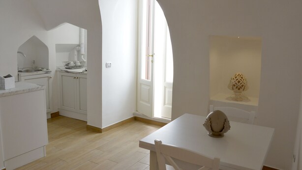 A kitchen with white cabinets, a dining table, and a window with natural light. - Casa Baldassarre (Ostuni)