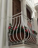 A white balcony with a white railing, potted plants with pink flowers, and a brown door.