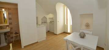 A modern kitchen with white cabinetry, a wooden floor, and a dining area with a white table and chairs.