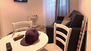 Uma sala de estar com televisão, sofá, mesa de centro e mesa de jantar com cadeiras.