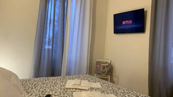 Ein Hotelzimmer mit einem Bett, einem Fernseher der 'NETFLIX' anzeigt, einem Sessel und einer Fernbedienung.
