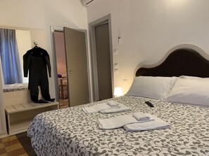 A hotel room with a bed, a bedside table, a hanging coat rack, and a door leading to another room. - Affittacamere LevantoMare (Levanto)