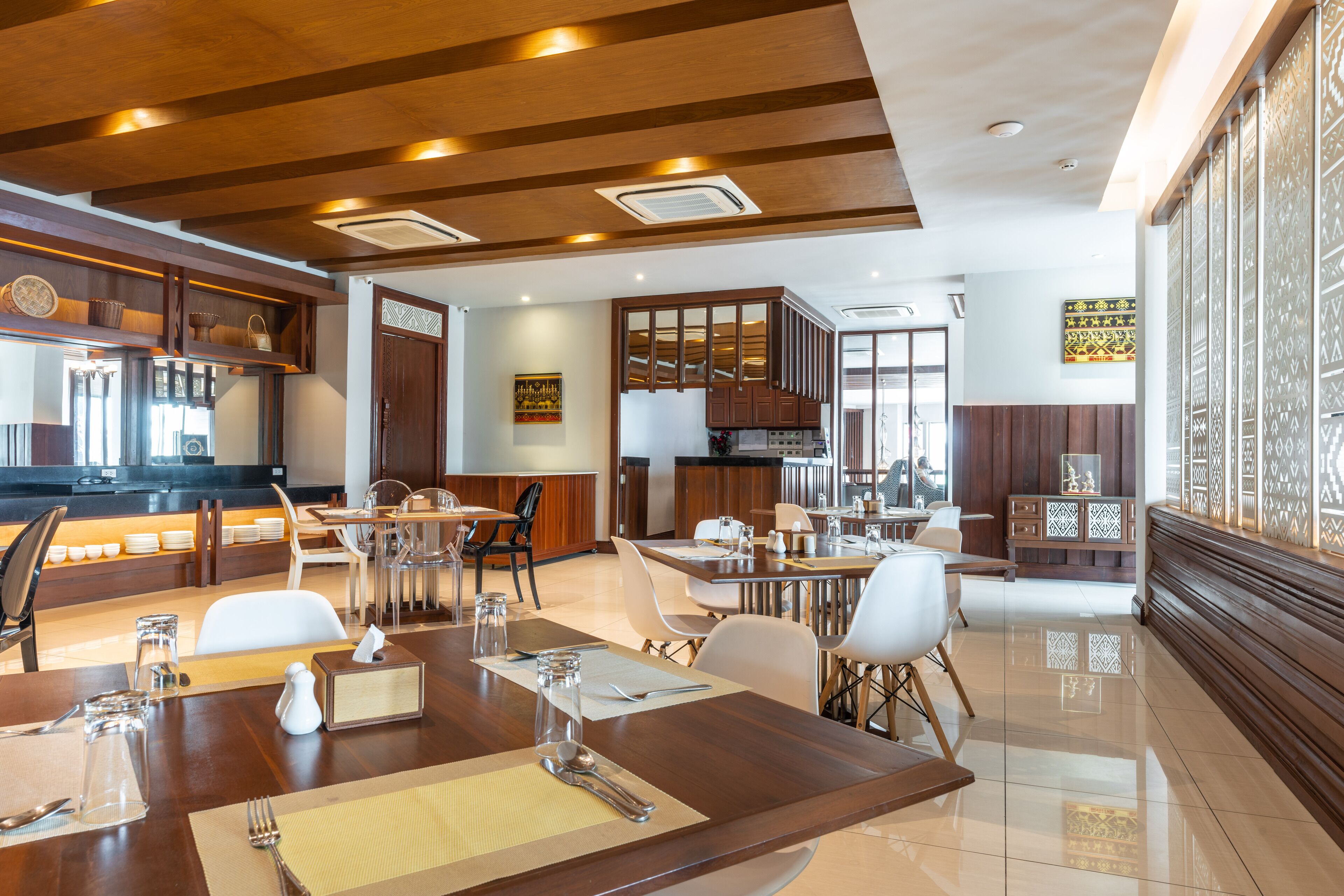 Un comedor de hotel moderno con vigas de madera en el techo, una cocina al fondo y un panel decorativo en la pared.