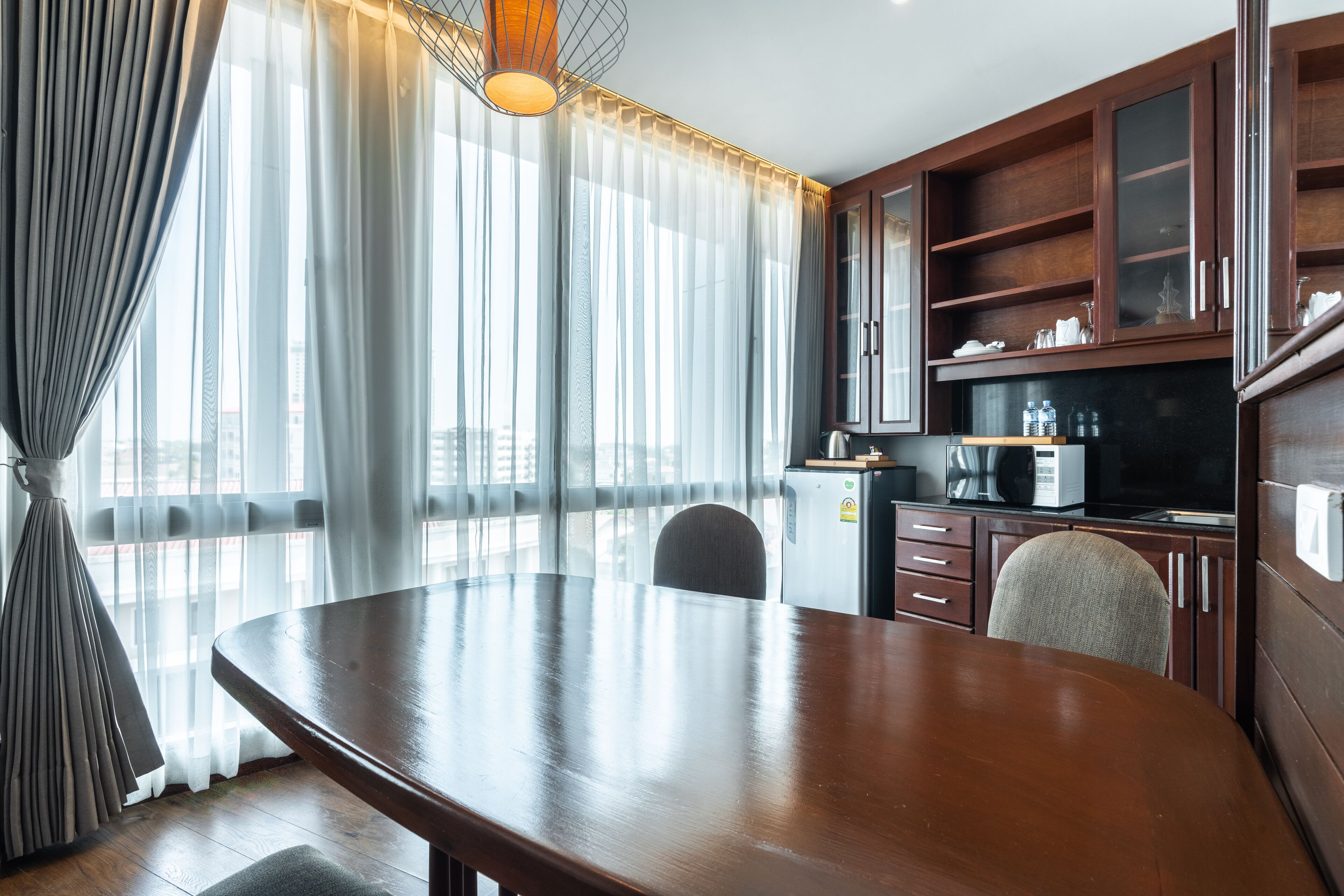 A modern kitchen with wooden cabinets, a dining table, and a large window with sheer curtains.