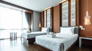 Habitación de hotel con dos camas, un ventanal grande con cortinas, un panel decorativo en la pared, una lámpara colgante y una mesita.