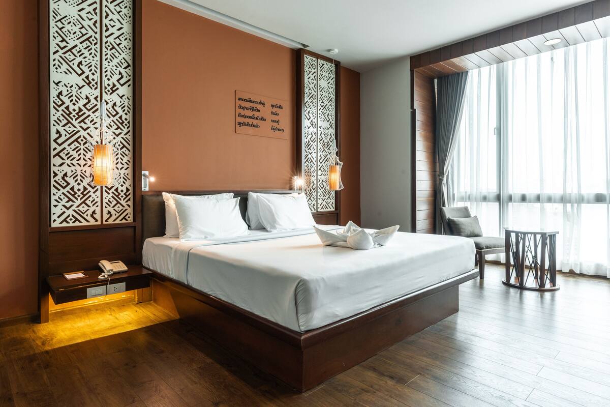 A modern hotel room with a large bed, bedside tables, a chair, and a small table.