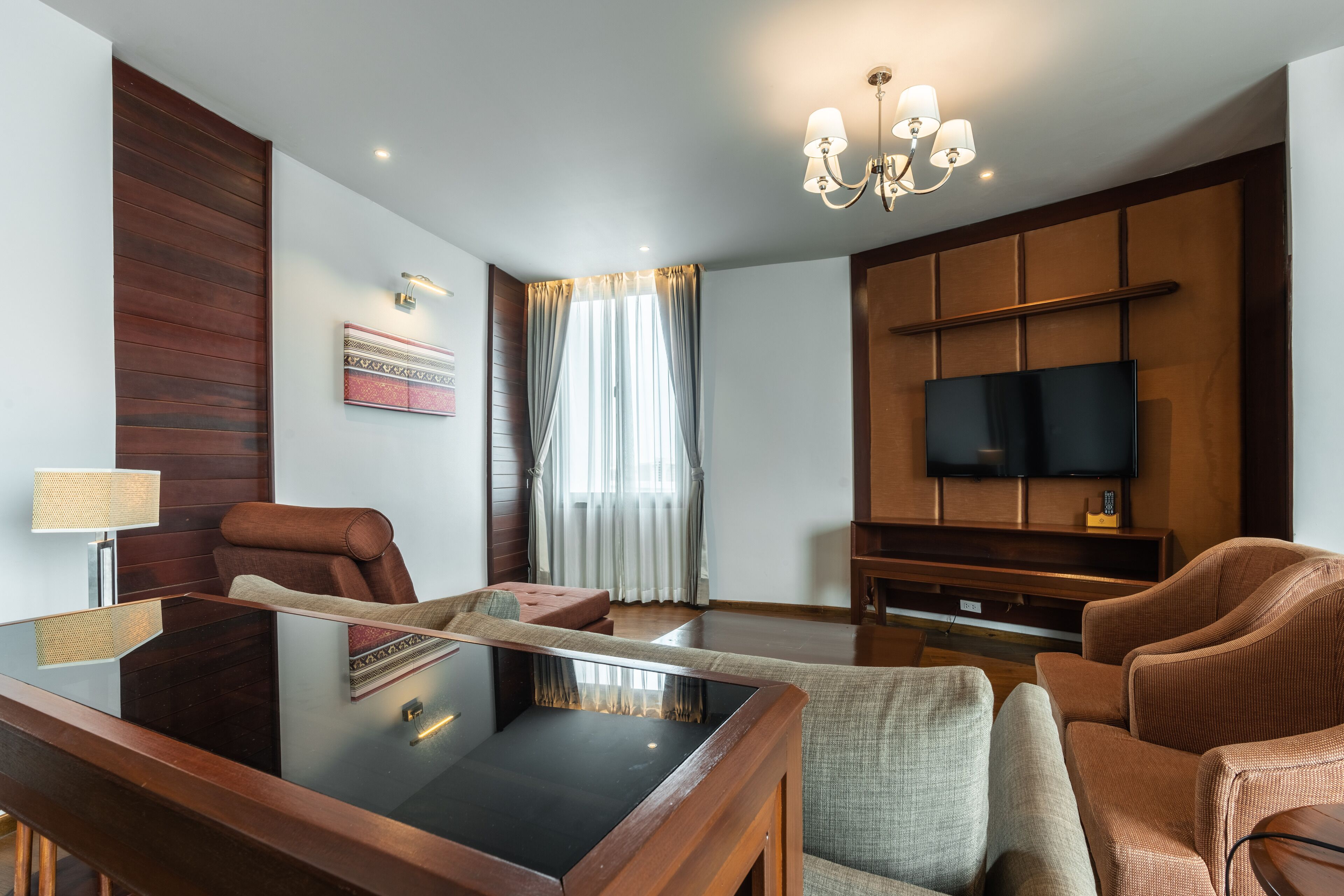 A modern living room with a glass coffee table, leather armchairs, a flat-screen TV, and a wooden accent wall.