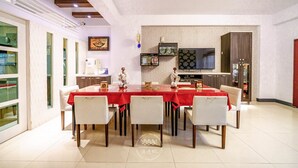 A dining area with a red table and white chairs, a television on the wall, and a kitchen area with cabinets and a refrigerator. - Sunny B&B (Ji'an)