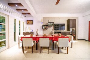 A dining area with a red table and white chairs, a television on the wall, and a kitchen area with cabinets and a refrigerator. - Sunny B&B (Ji'an)
