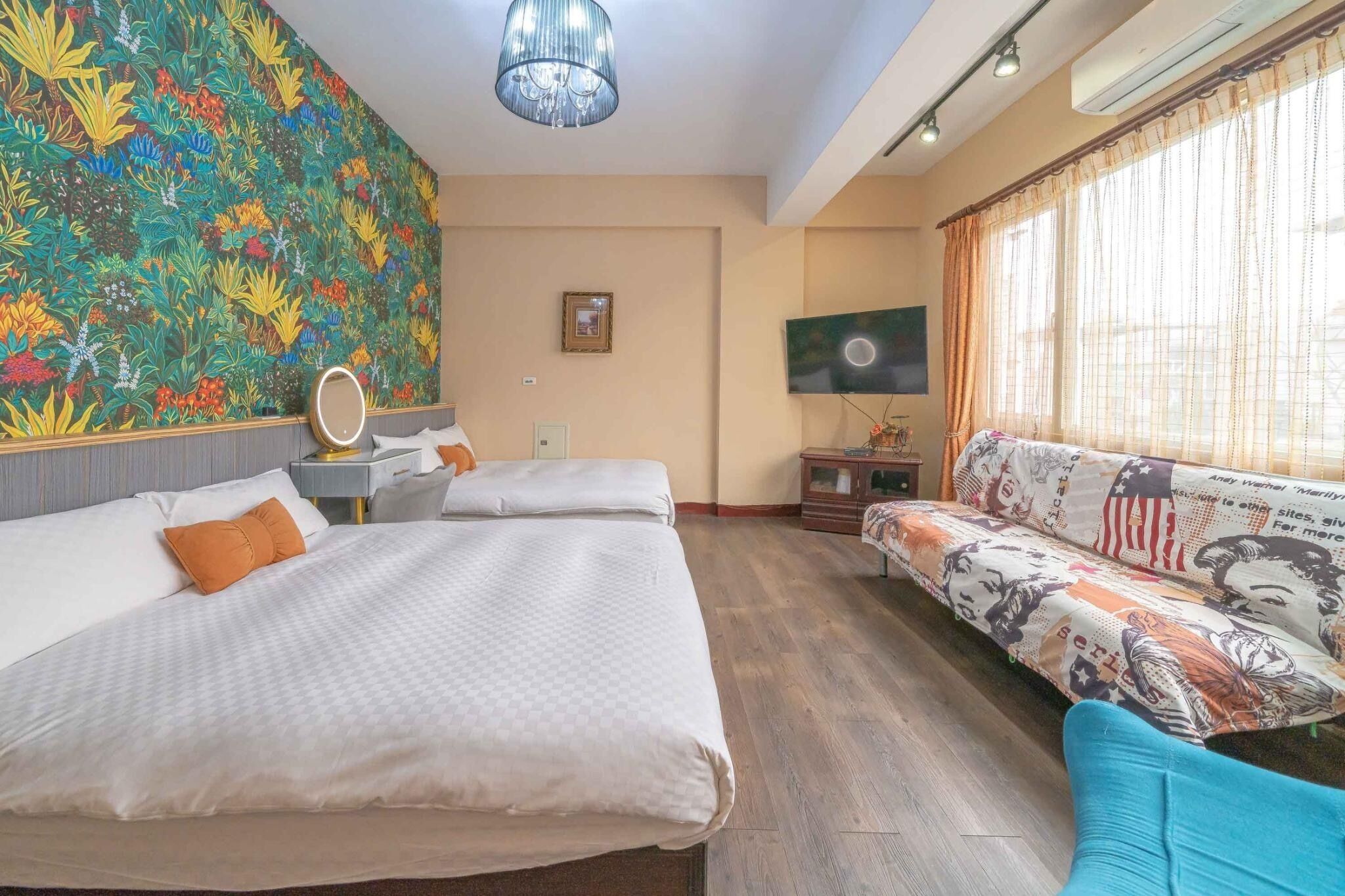 A hotel room with a large bed, a sofa, a TV, and a colorful floral wall.
