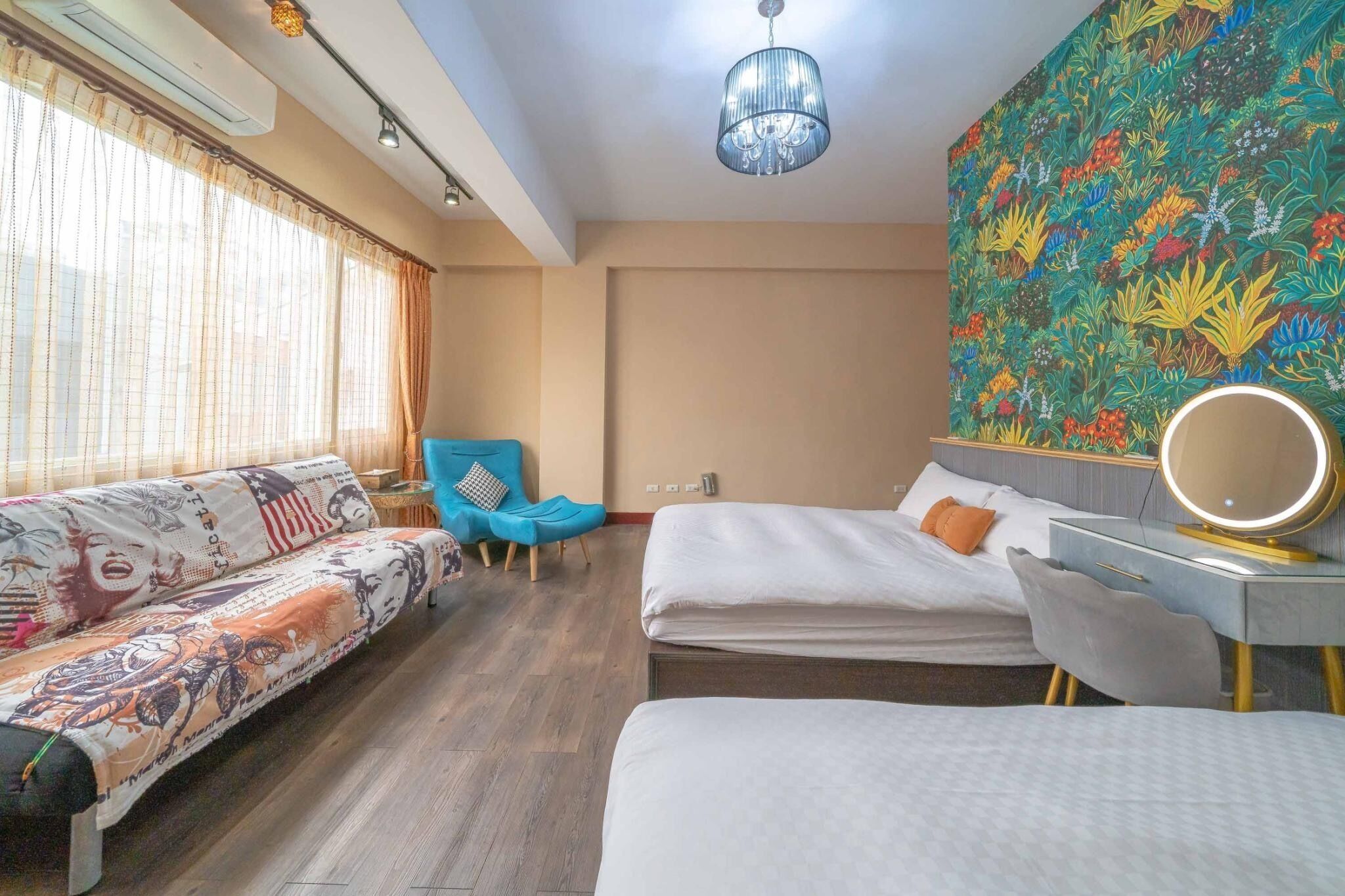 A hotel room with a bed, a sofa, a desk with a mirror, and a colorful floral wall.