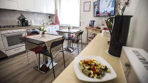 Una cocina moderna con armarios blancos, una mesa de comedor con sillas, un televisor montado en la pared y un plato de bombones sobre la mesa.