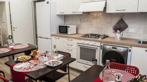 Una cocina moderna con armarios blancos, microondas, estufa, horno y lavadora. Hay una mesa de comedor con sillas y una pequeña mesa con un jarrón y flores.