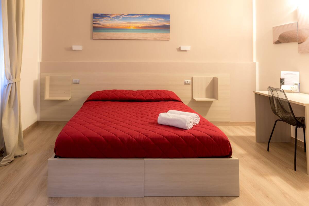Una habitación de hotel moderna con una cama roja, un escritorio y una silla.