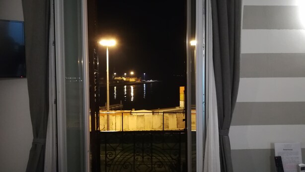 Een balkon met een metalen hekwerk, uitzicht op een steiger met boten, en een stadsgezicht in de nacht.