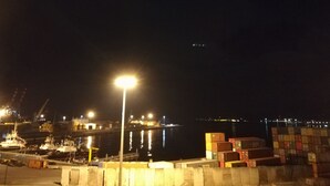 Een haven bij nacht, met boten, containers en een felle lantaarnpaal.