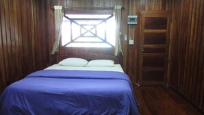 A bedroom with a wooden paneled wall, a bed with a blue bedspread, a window with curtains, and a wooden door. - Pialo Resort (Na Klang)