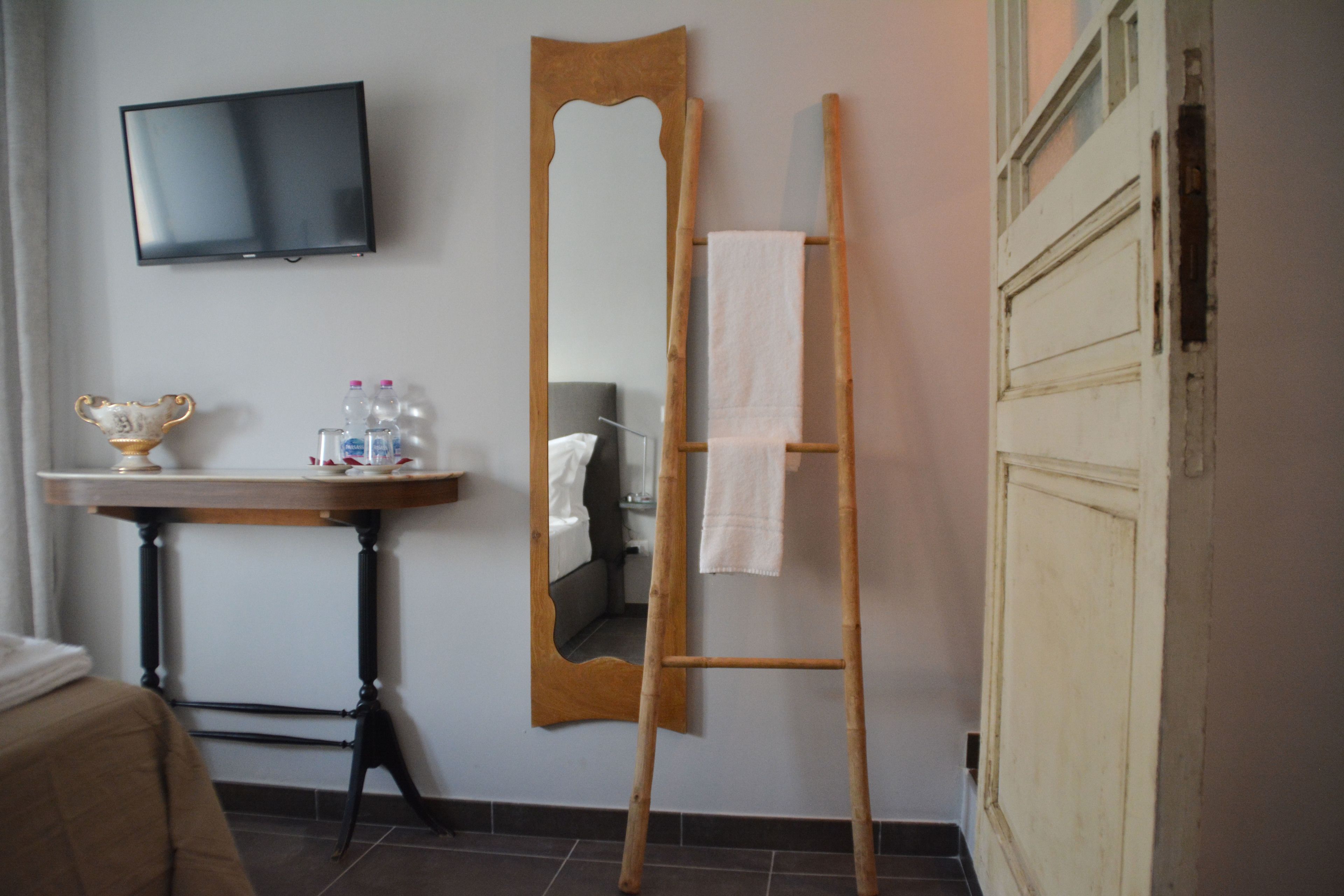 A bathroom with a wooden ladder, a large mirror, a television mounted on the wall, and a small table with toiletries.