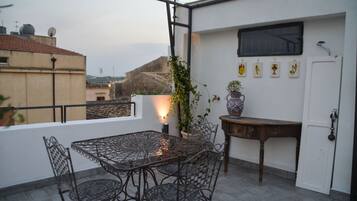 A rooftop terrace with a metal table and chairs, a potted plant, and a small table with a vase.