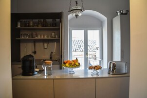 Una cocina con frutero, cafetera, tostadora y ventana con vista a un edificio.