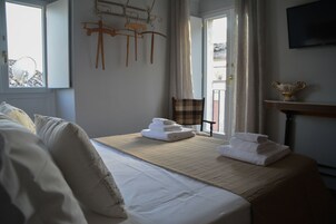Habitación de hotel con cama, una mesa con toallas, una silla, televisor y ventana con cortinas.