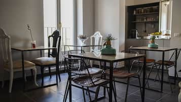 Uma área de refeições com mesa e cadeiras, uma planta em vaso e uma cozinha ao fundo.