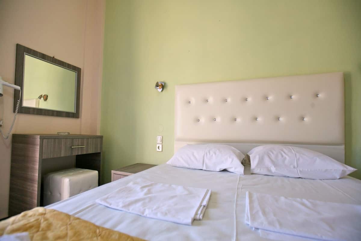 A hotel room with a large bed, a bedside table, a mirror, and a wall-mounted phone.