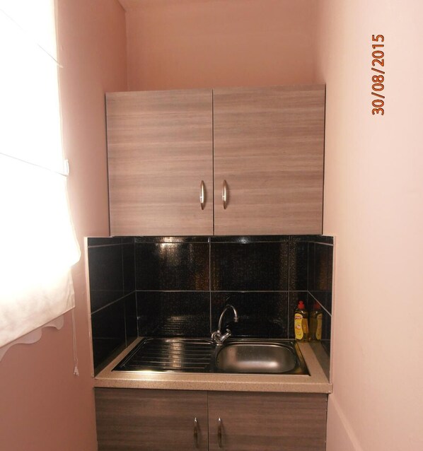A compact kitchen with two cabinets, a sink, and black tiles.